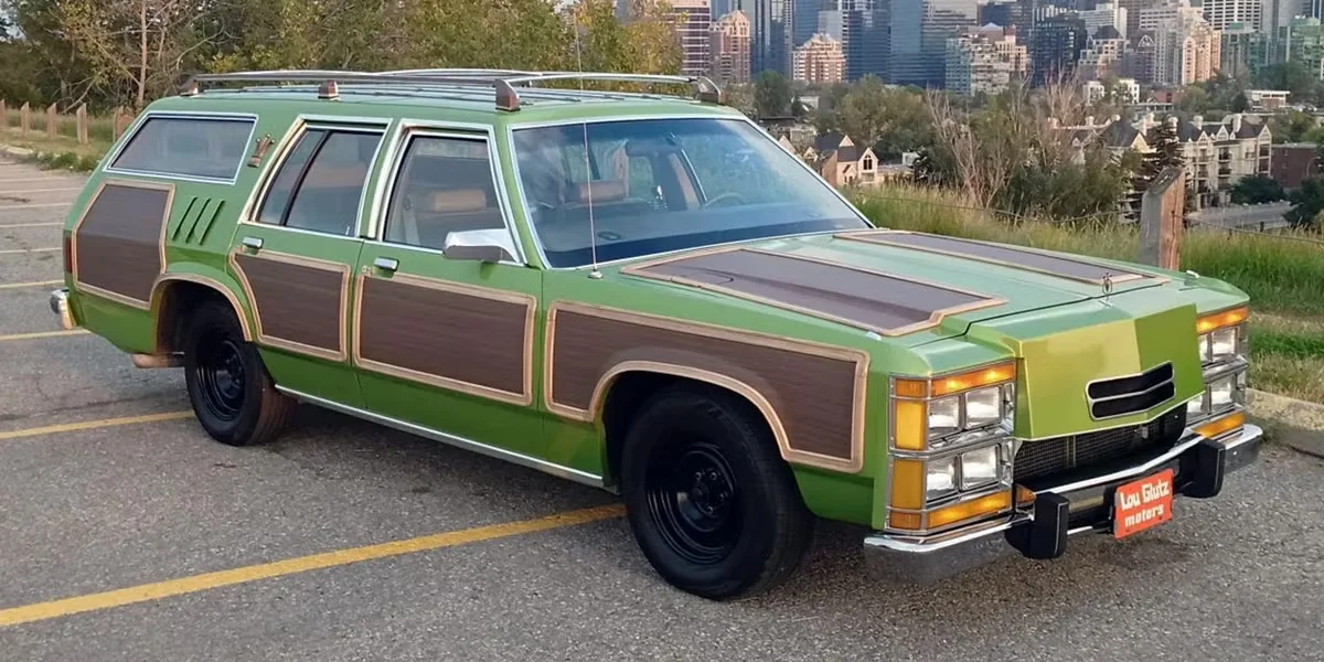 A Wagon Queen Family Truckster replica: a station wagon in Metallic Pea green with fake woodgrain side panelling, a roof rack, and four stacked pairs of headlights across the front.